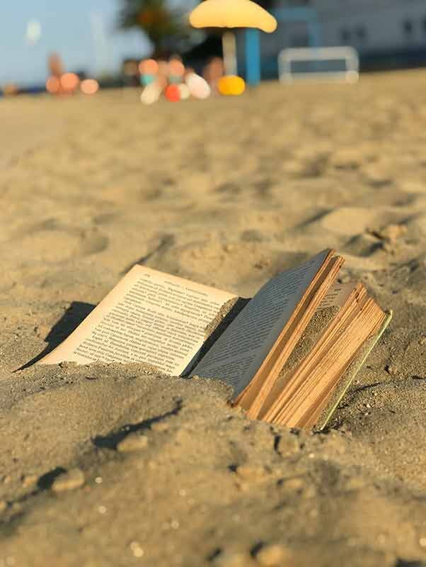 An open Latin book filled with sand on a beach.